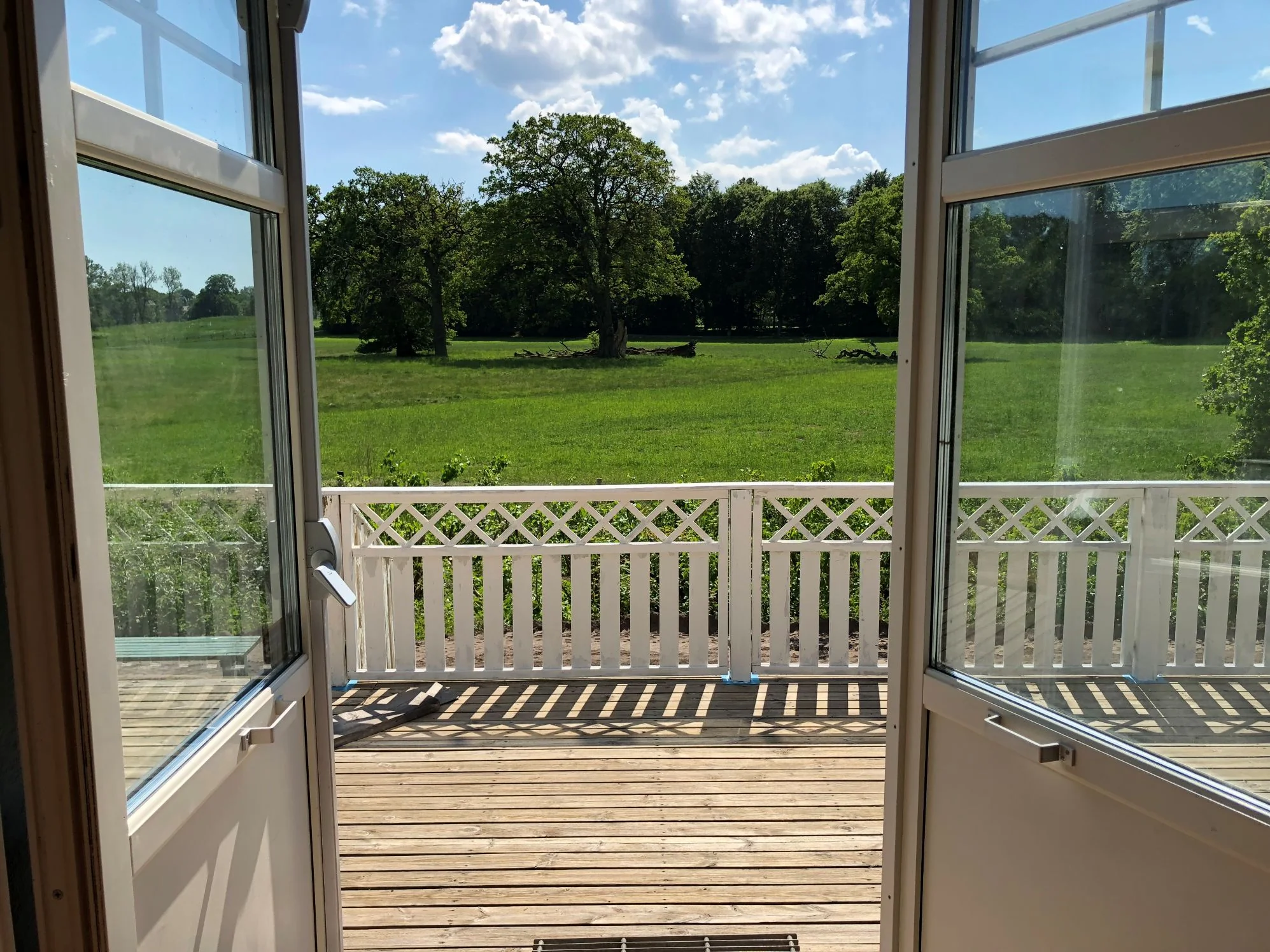 Dörrarna till verandan står halvöppna och ängen med träd syns.